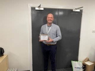 A man holding a Healthwatch Sunderland star award certificate smiling at the camera