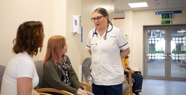 A nurse standing talking to two women in a waiting room