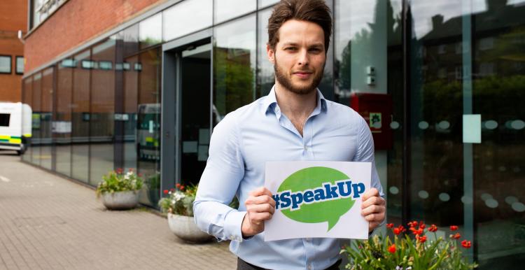 Man holding a sign outside a hospital that says 'Speak Up' Man holding a sign outside a hospital that says 'Speak Up'