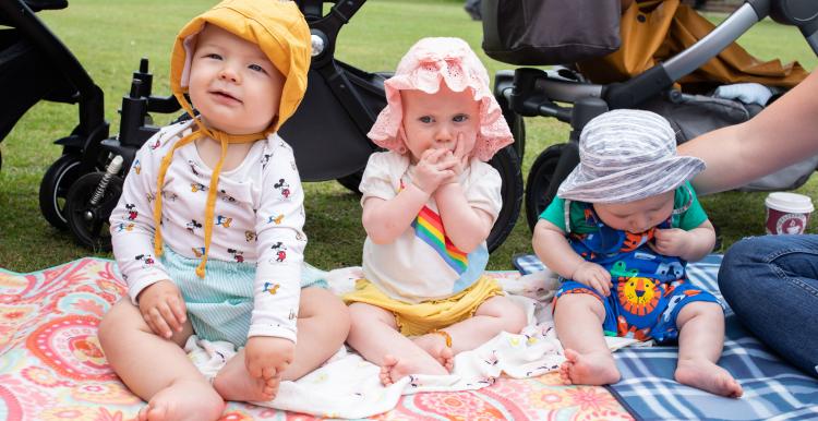 Three babies at a picnic in the park sitting on a blanket