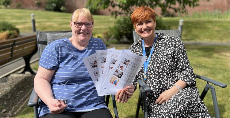 Two women sitting in a chair holding papers smiling at the camera