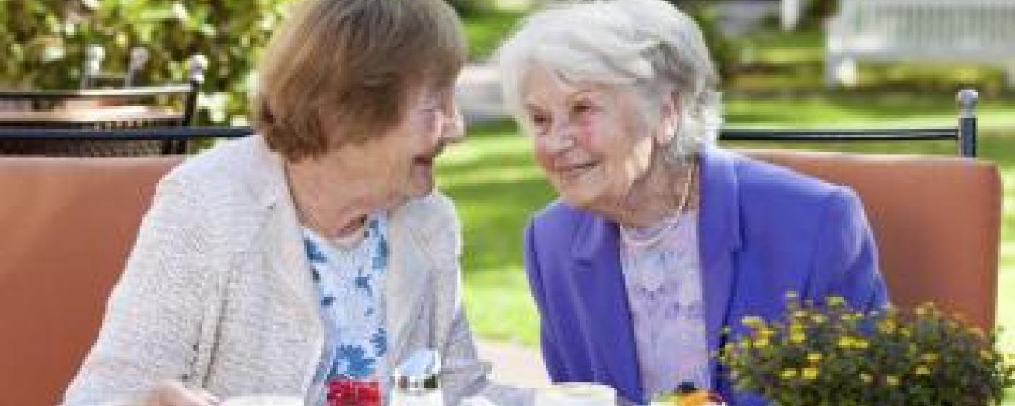 Two woman smiling at each other drinking a cup of tea