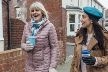 Two women walking down a street drinking coffee