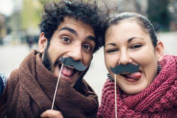 A man and a woman holding a false mustache