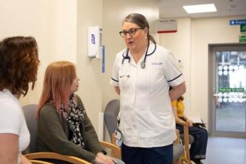 A nurse standing talking to two women in a waiting room