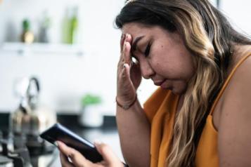 Worried mid adult woman of colour using a mobile phone in the living room at home