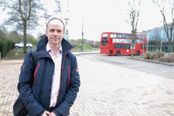 Man stood outside near a roundabout and in front of a bus