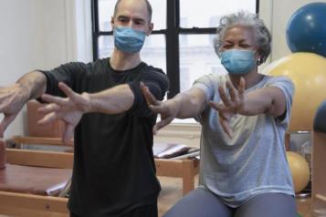 A man and a woman sitting on exercise balls. Their arms are stretched out in front of them.