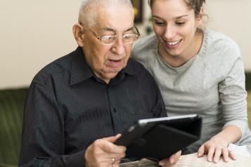 Young woman helping an elderly gentleman work a tablet