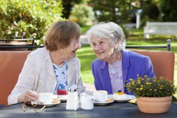 Two woman smiling at each other drinking a cup of tea