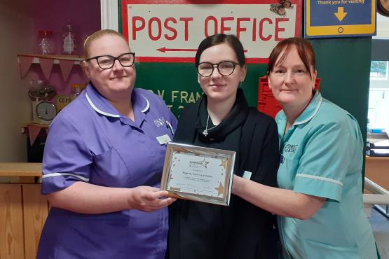 Three ladies holding a certificate and looking at the camera