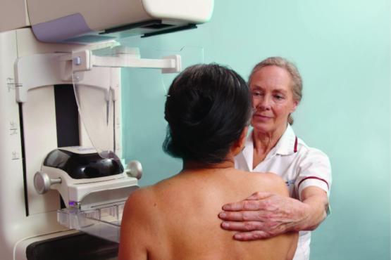 Woman standing next to mammography equipment, being helped into position by a female mammographer