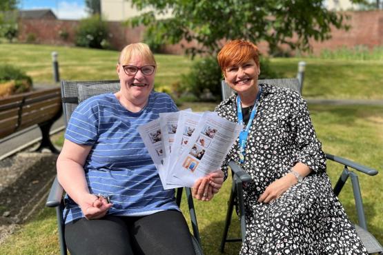 Two women sitting in a chair holding papers smiling at the camera