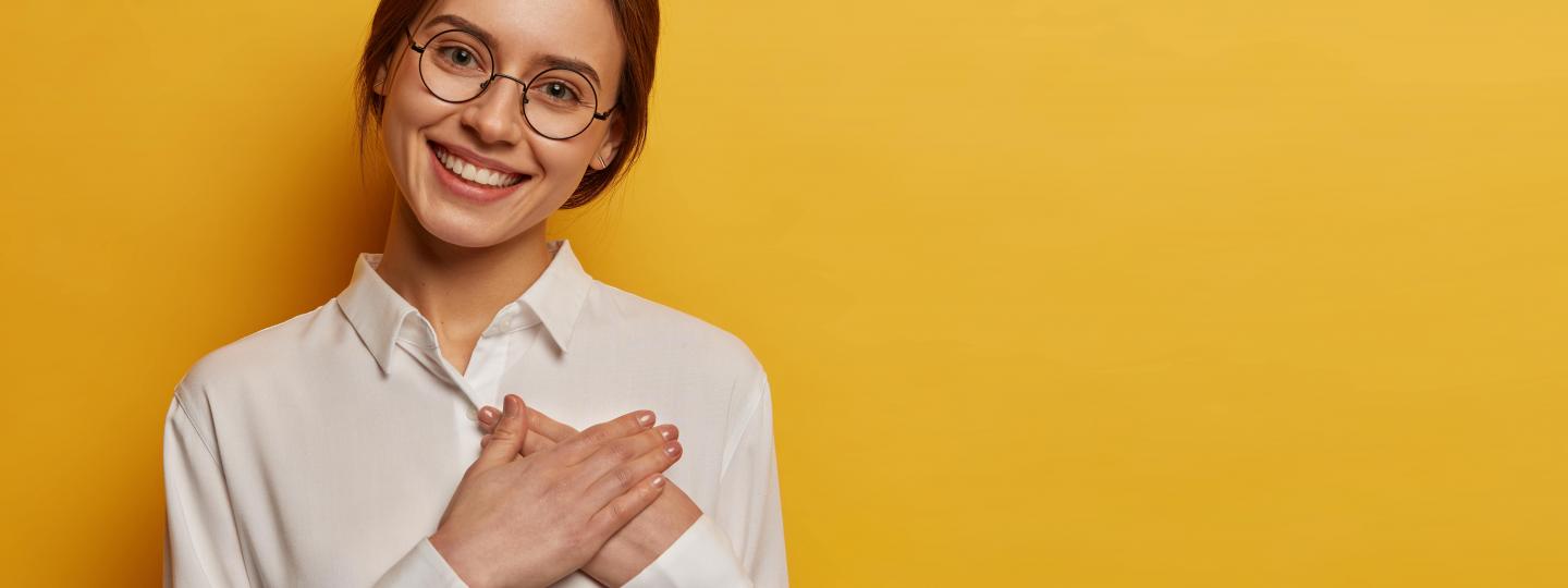 Charming positive woman presses hands to chest to gesture thank you