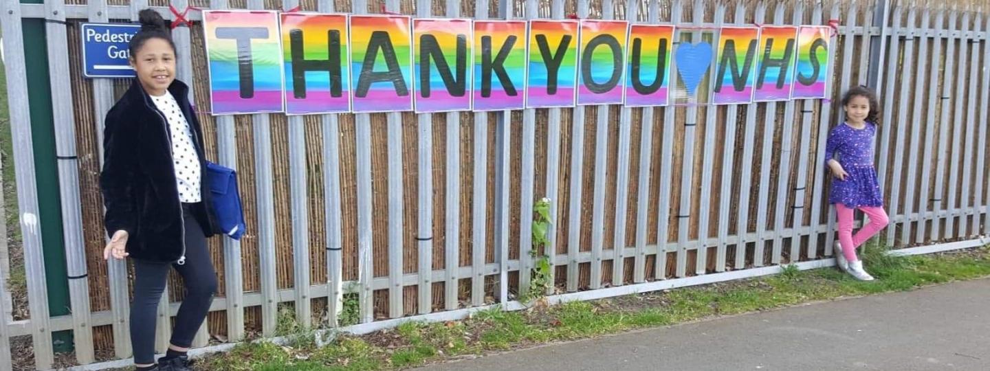Two children standing next to a fence with a thank you banner