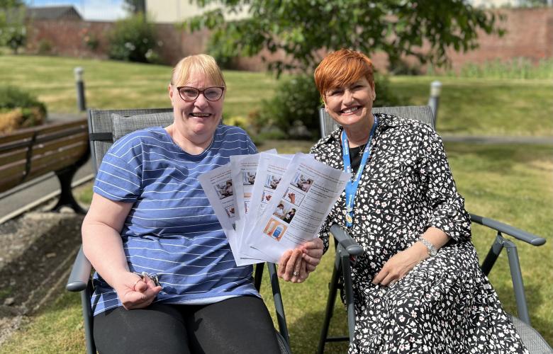 Two women sitting in a chair holding papers smiling at the camera